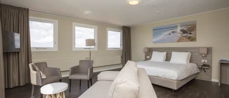 A modern hotel room with a large bed, two armchairs, a sofa, a TV, and a painting of a seagull on the wall.
