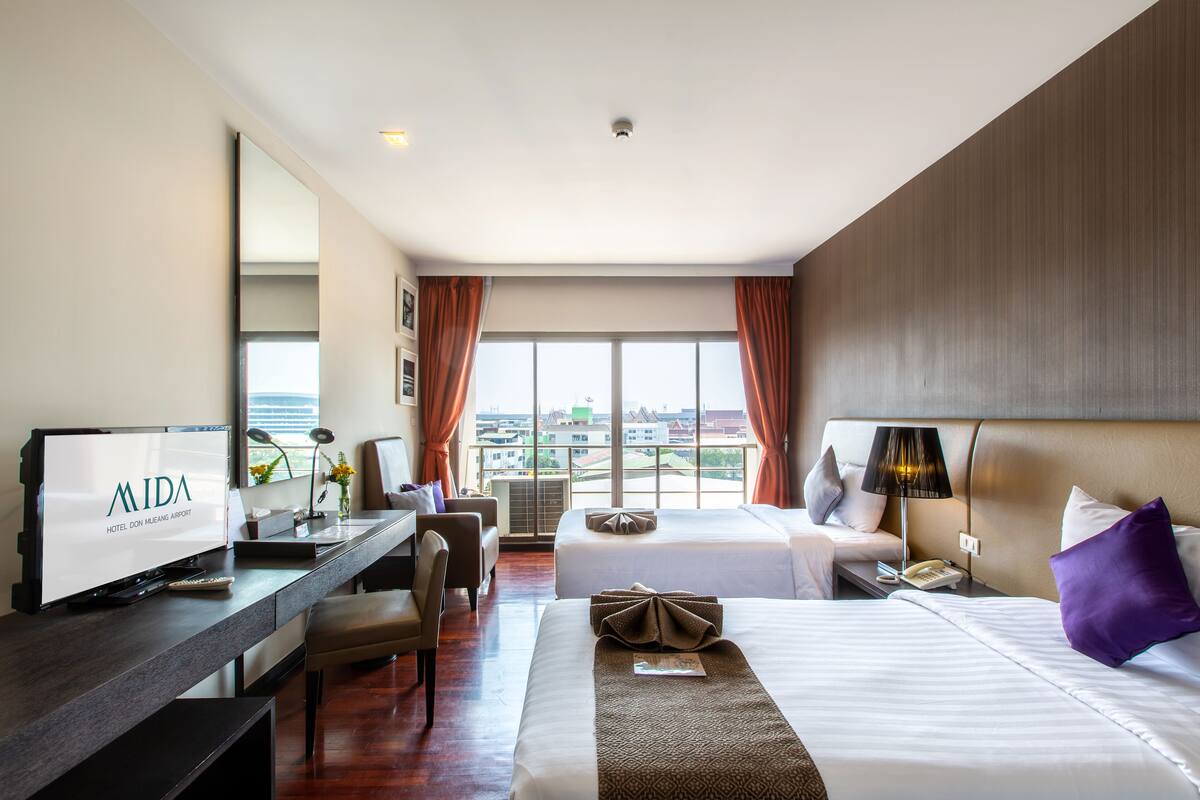 A hotel room with a large bed, a desk with a computer, a chair, and a view of the city.
