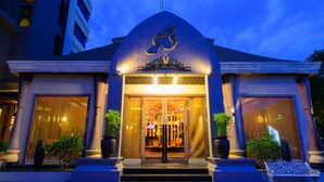 A hotel entrance with a large glass facade, a decorative archway, and a sign above the door. - Mida Hotel Don Mueang Airport (Bangkok)