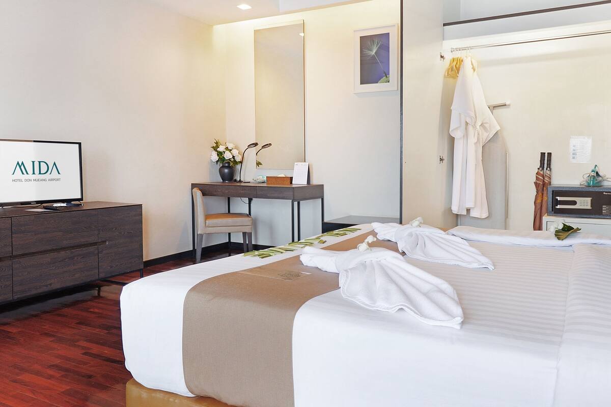 A hotel room with a bed, a desk, a chair, a TV, and a mirror.