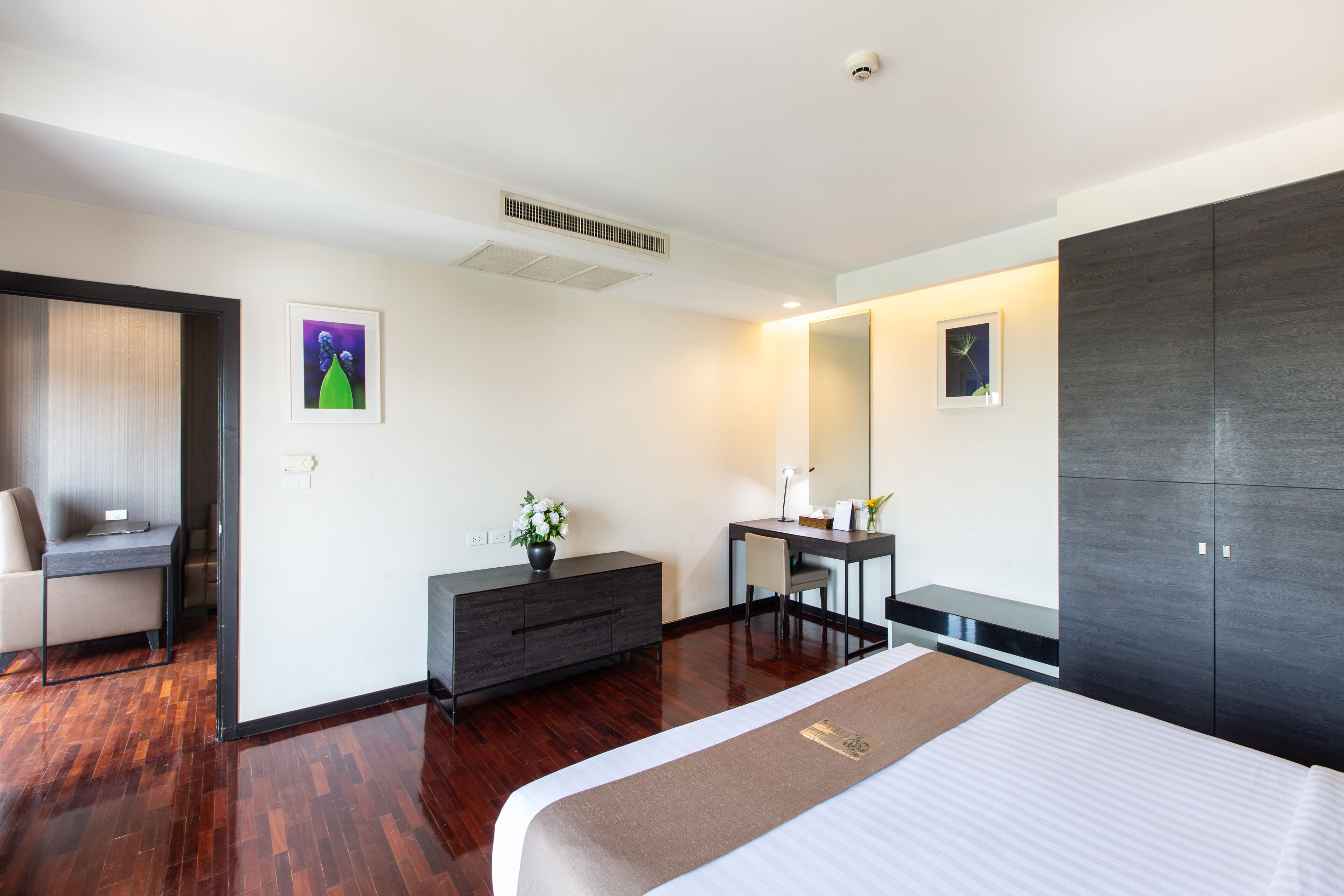 A modern hotel room with a large bed, a desk, a chair, a dresser, and a large mirror.