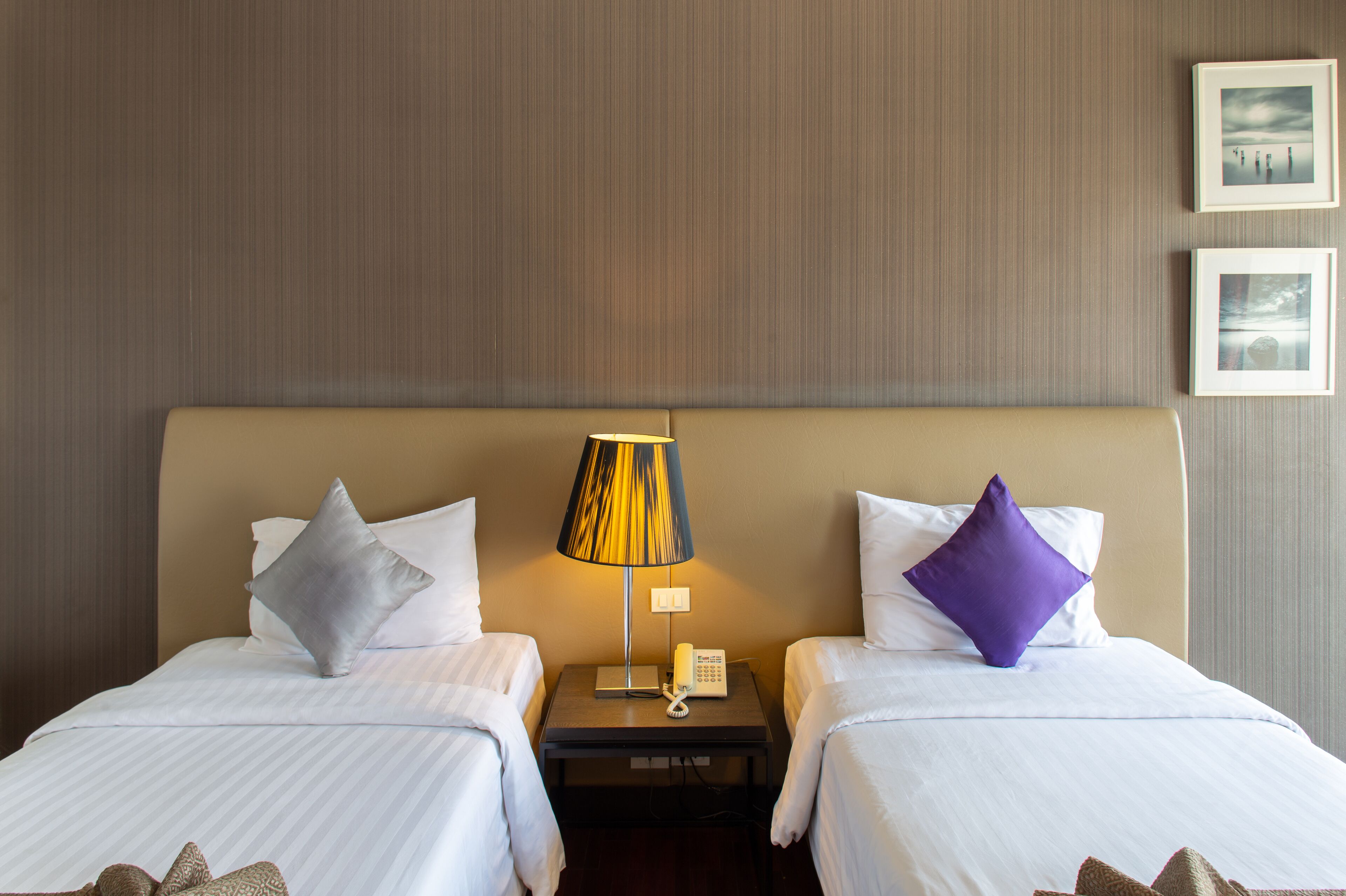 Een hotelkamer met twee bedden, een nachtkastje met een lamp en twee ingelijste foto's aan de muur.