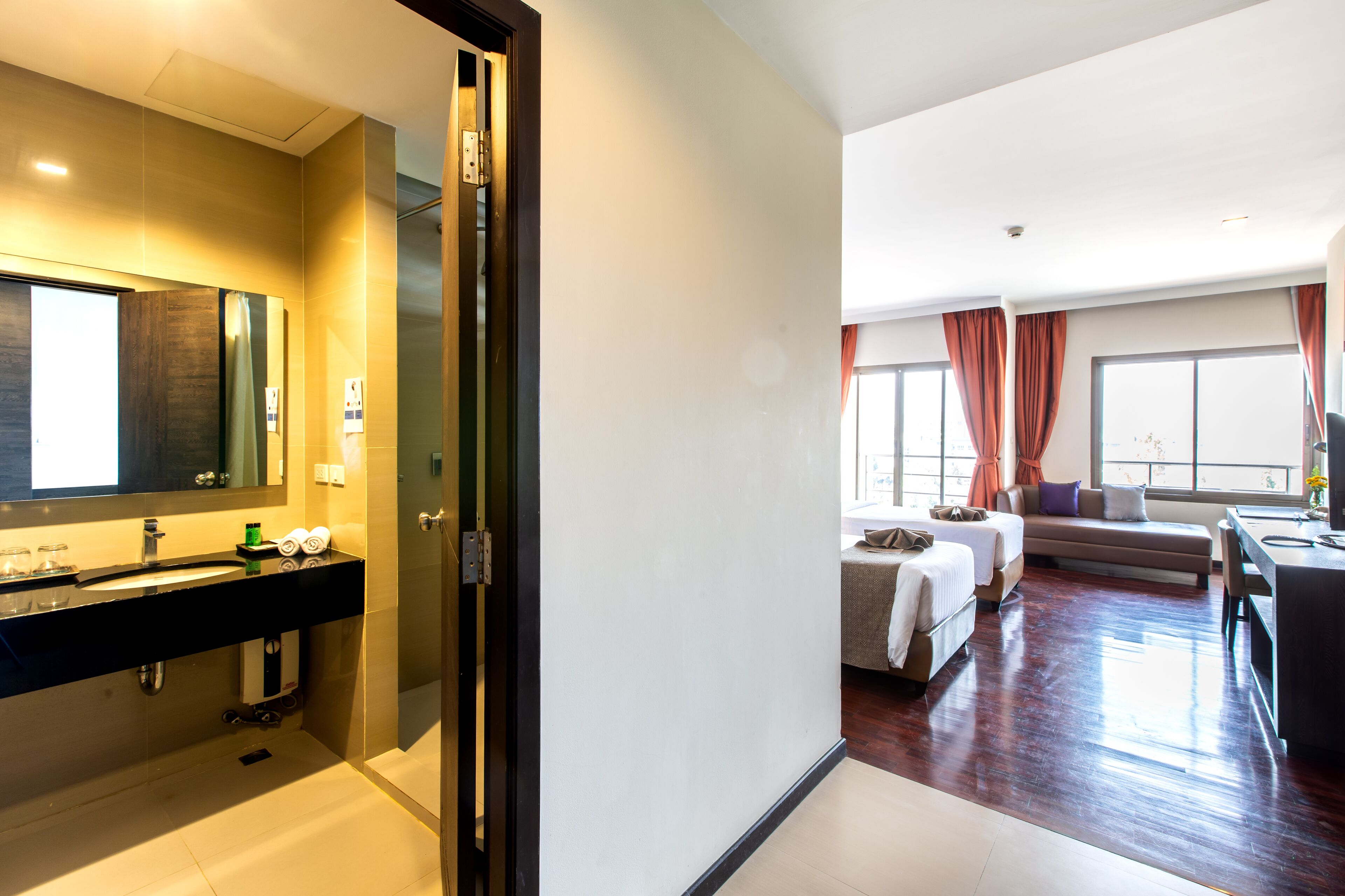 Een hotelkamer met een badkamer, een zithoek met een bank en een tafel, en een groot raam met gordijnen.