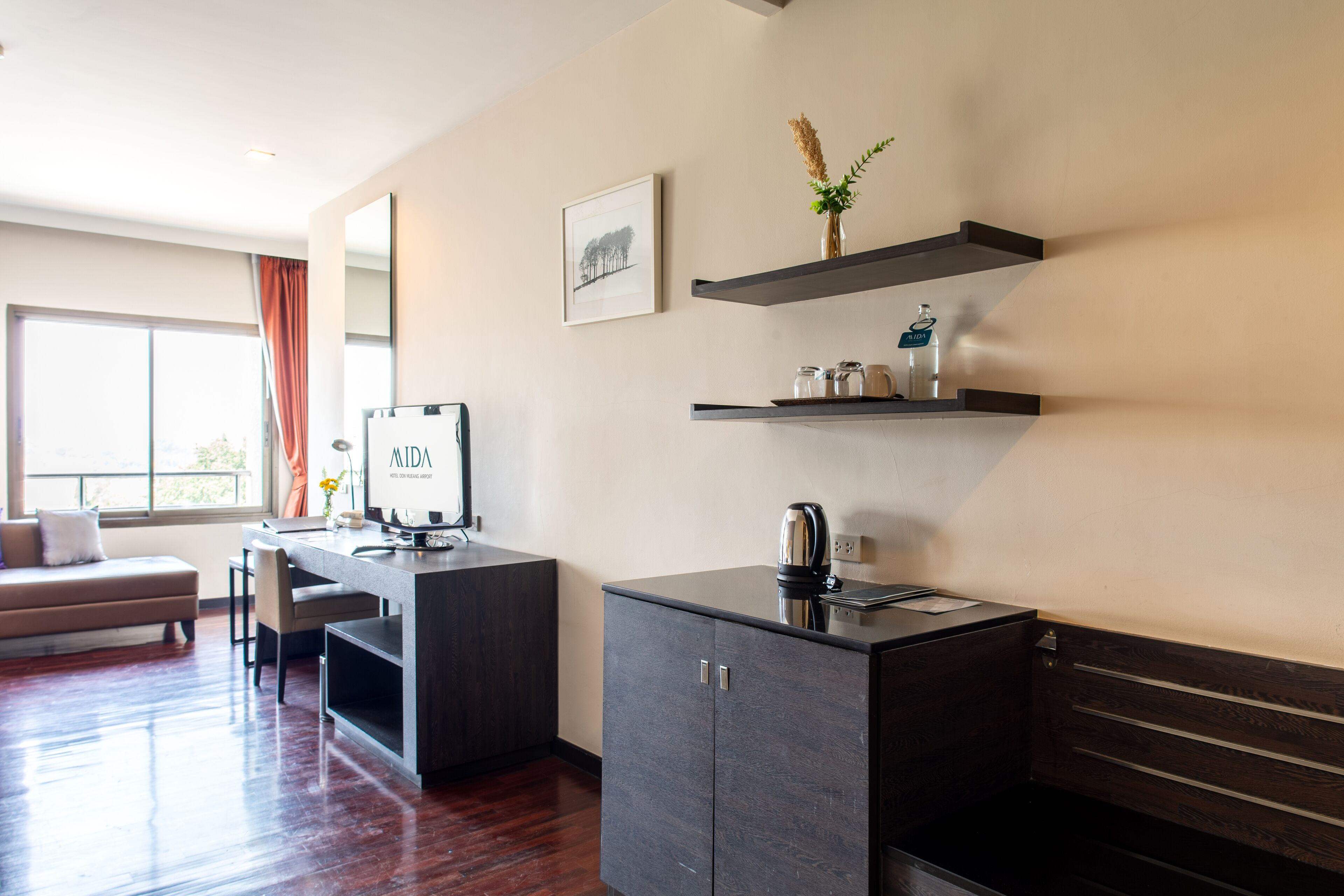 A modern hotel room with a dark wood cabinet, a desk with a computer, and a window with curtains.