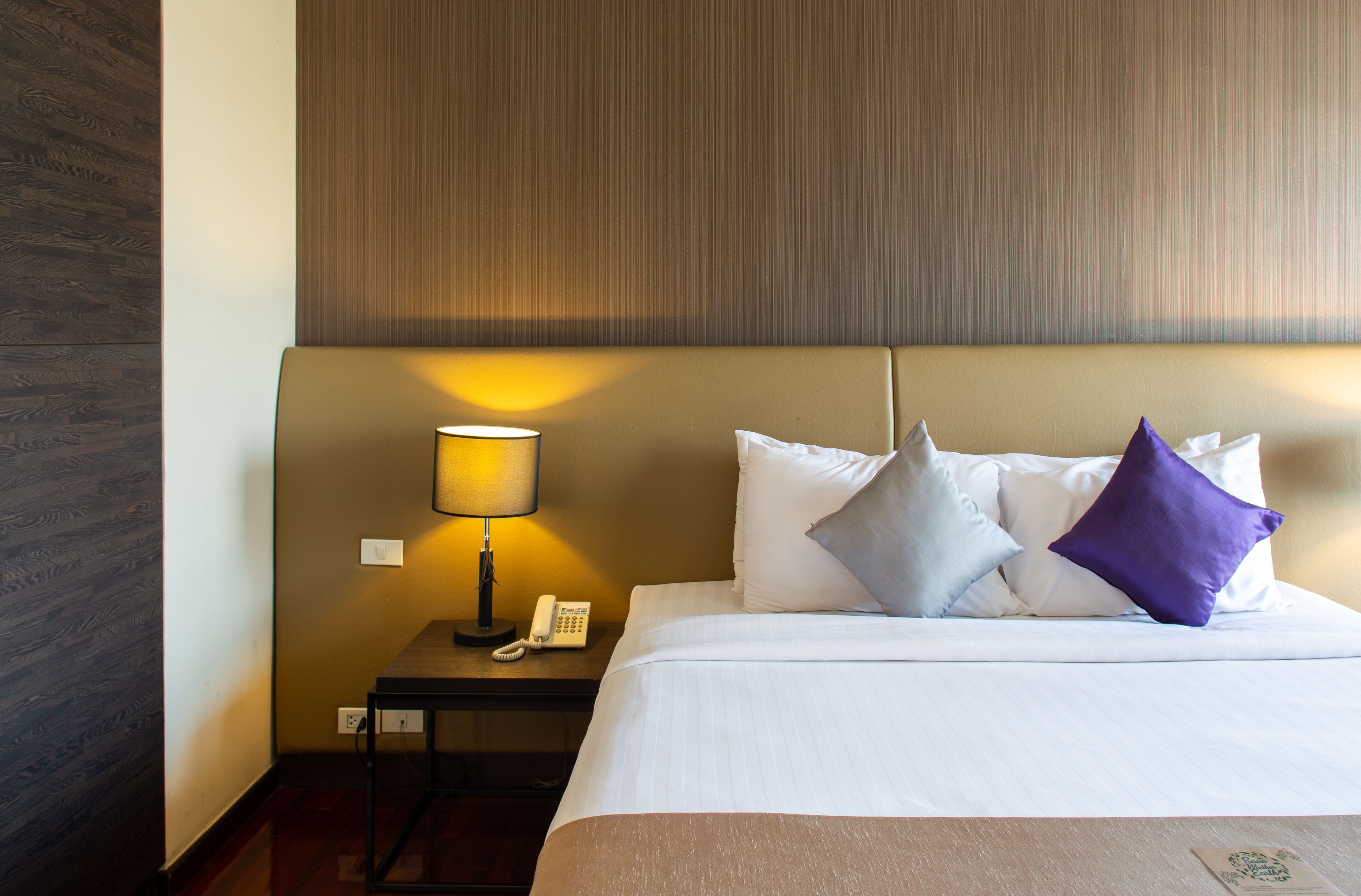 A hotel room with a bed, a nightstand with a lamp, and a telephone.