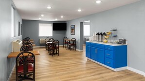Un comedor con mesas y sillas de madera, una barra azul con servicios y un televisor de pantalla plana en la pared.
