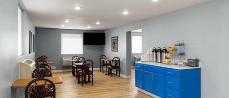 A dining area with wooden tables and chairs, a blue counter with amenities, and a flat-screen TV on the wall.