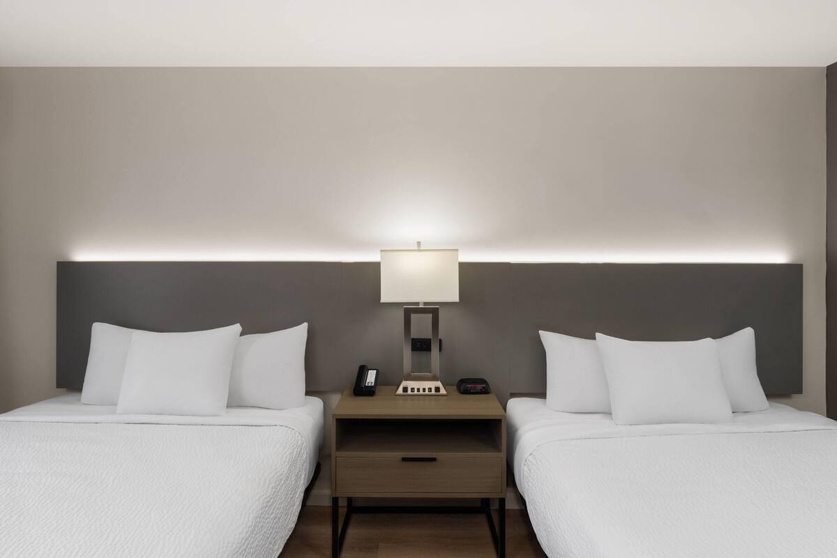 Una camera d'albergo con due letti singoli, un comodino con una lampada, un telefono e un tavolino.