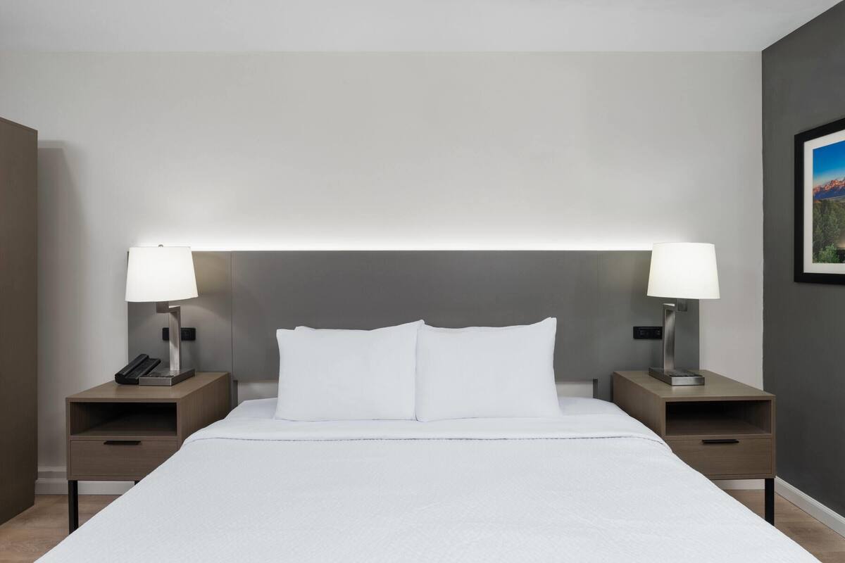 Un letto rifatto con lenzuola bianche, due comodini con lampade e un quadro appeso al muro.