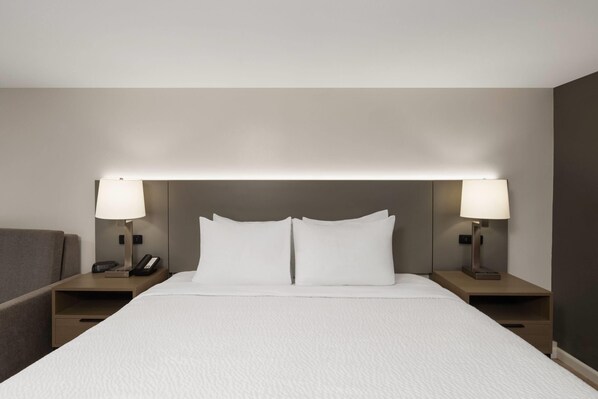 Cama bem arrumada com lençóis brancos, duas luminárias de cabeceira e um telefone em uma mesa de cabeceira de madeira.