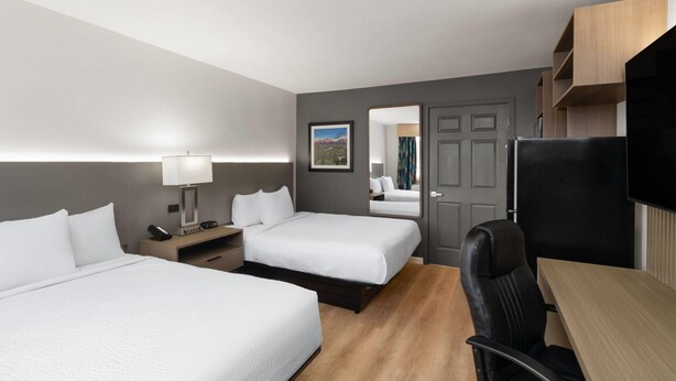 Habitación de hotel con dos camas, un escritorio, una silla, un televisor, un espejo y una puerta.