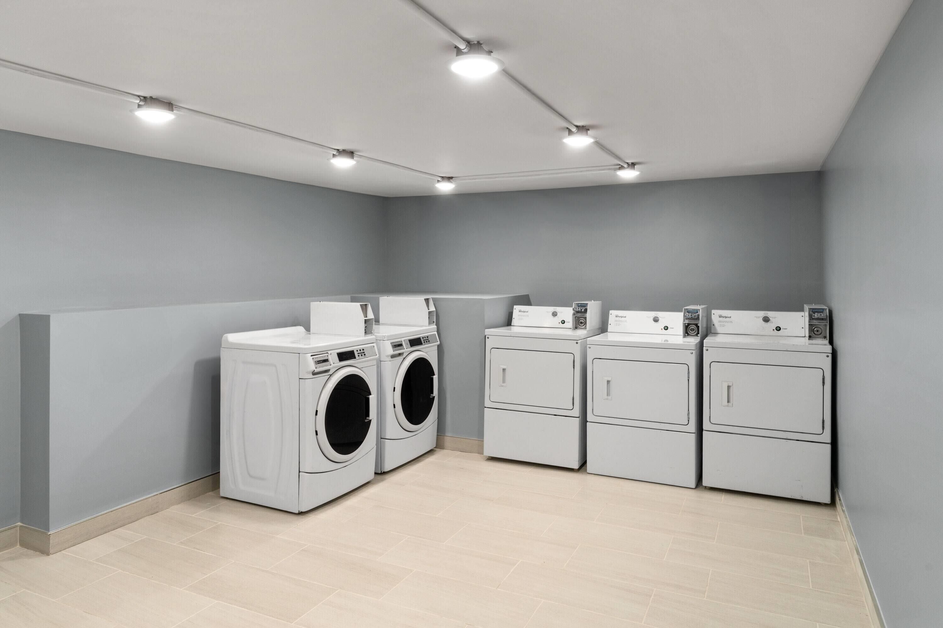 A laundry room with four washing machines and two dryers, equipped with overhead lighting.