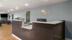 Un mostrador de recepción con una computadora portátil, una computadora de escritorio y un teléfono. Hay un letrero en la pared con el nombre "Baymont by Wyndham".