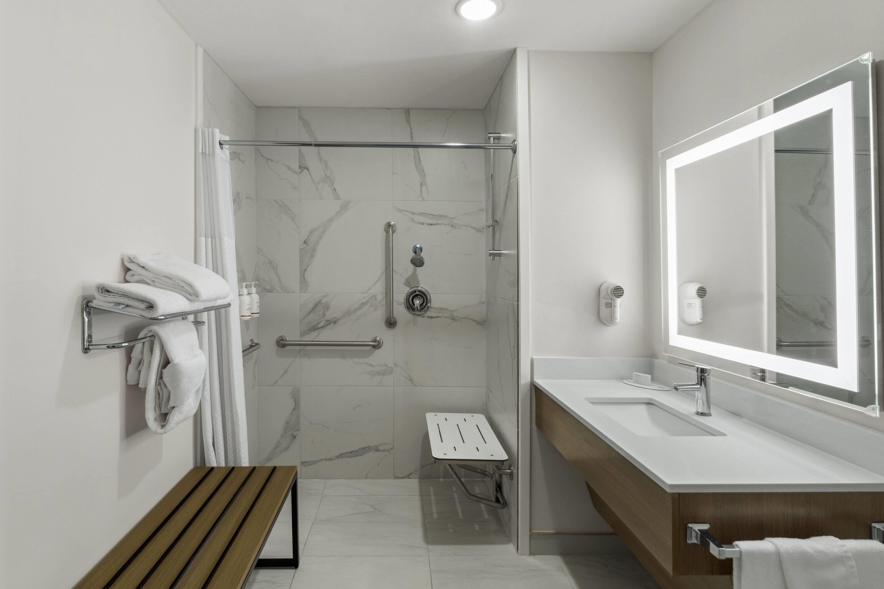 Une salle de bain moderne équipée d’une douche, d’un banc, d’un meuble-lavabo avec un grand miroir et d’un porte-serviettes.