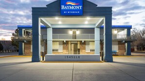 Un hotel Baymont con un llamativo esquema de colores azul y blanco, una entrada grande con marquesina, y el número 1545ELK exhibido debajo.