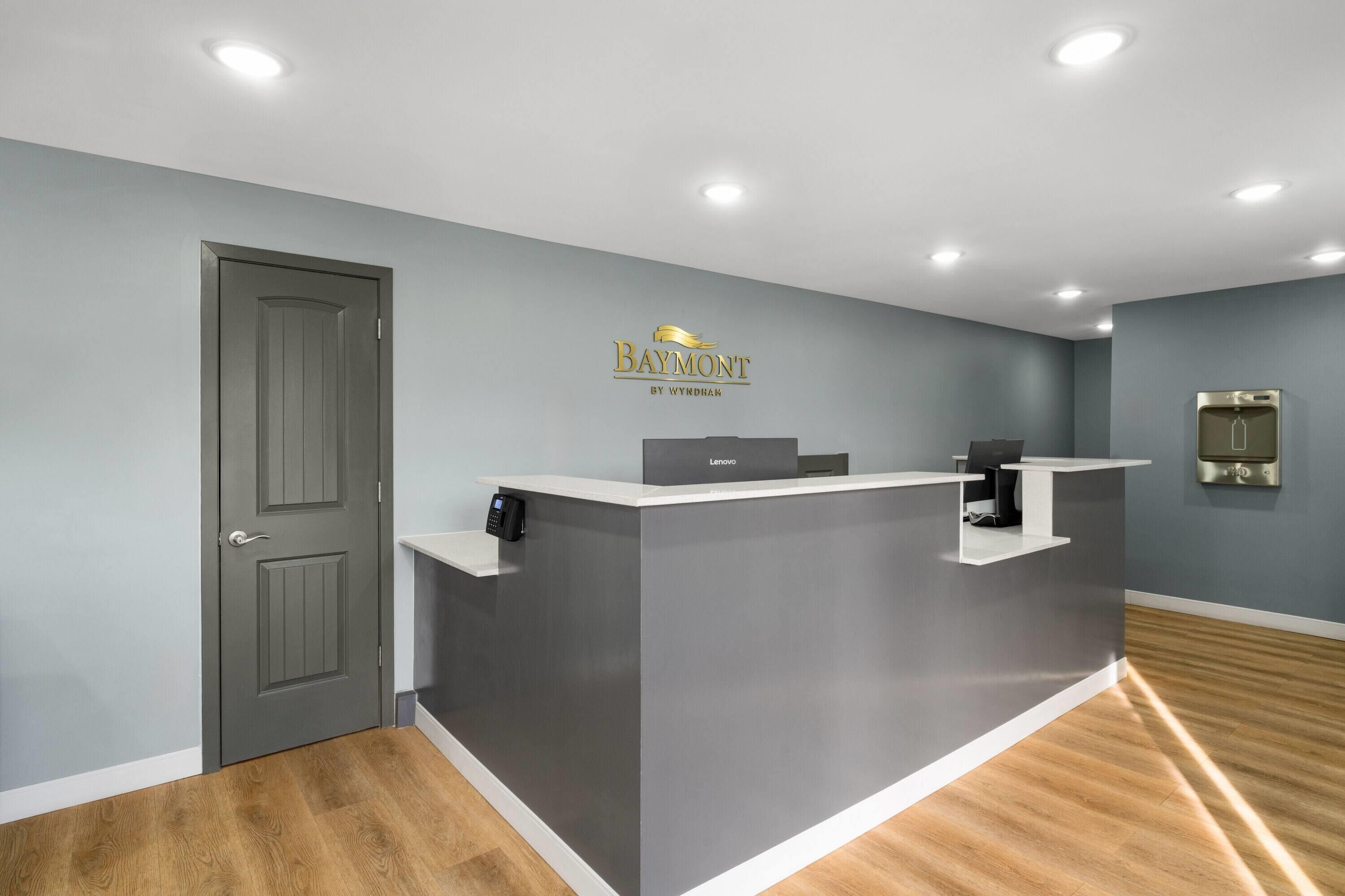 A reception desk with a grey finish, a door to the left, and a wall-mounted thermostat.