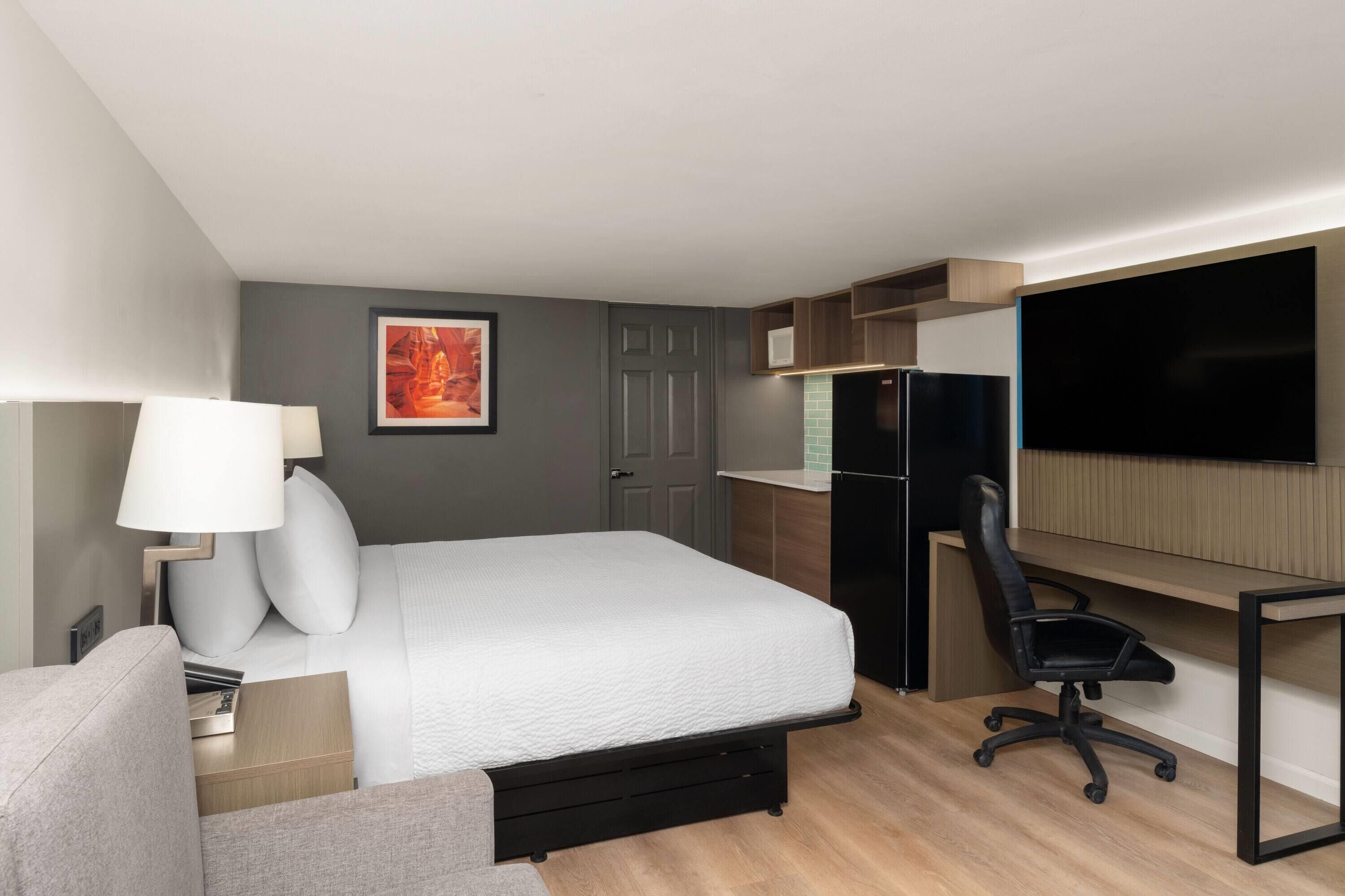 Habitación de hotel con cama, escritorio, silla, televisión y refrigerador.