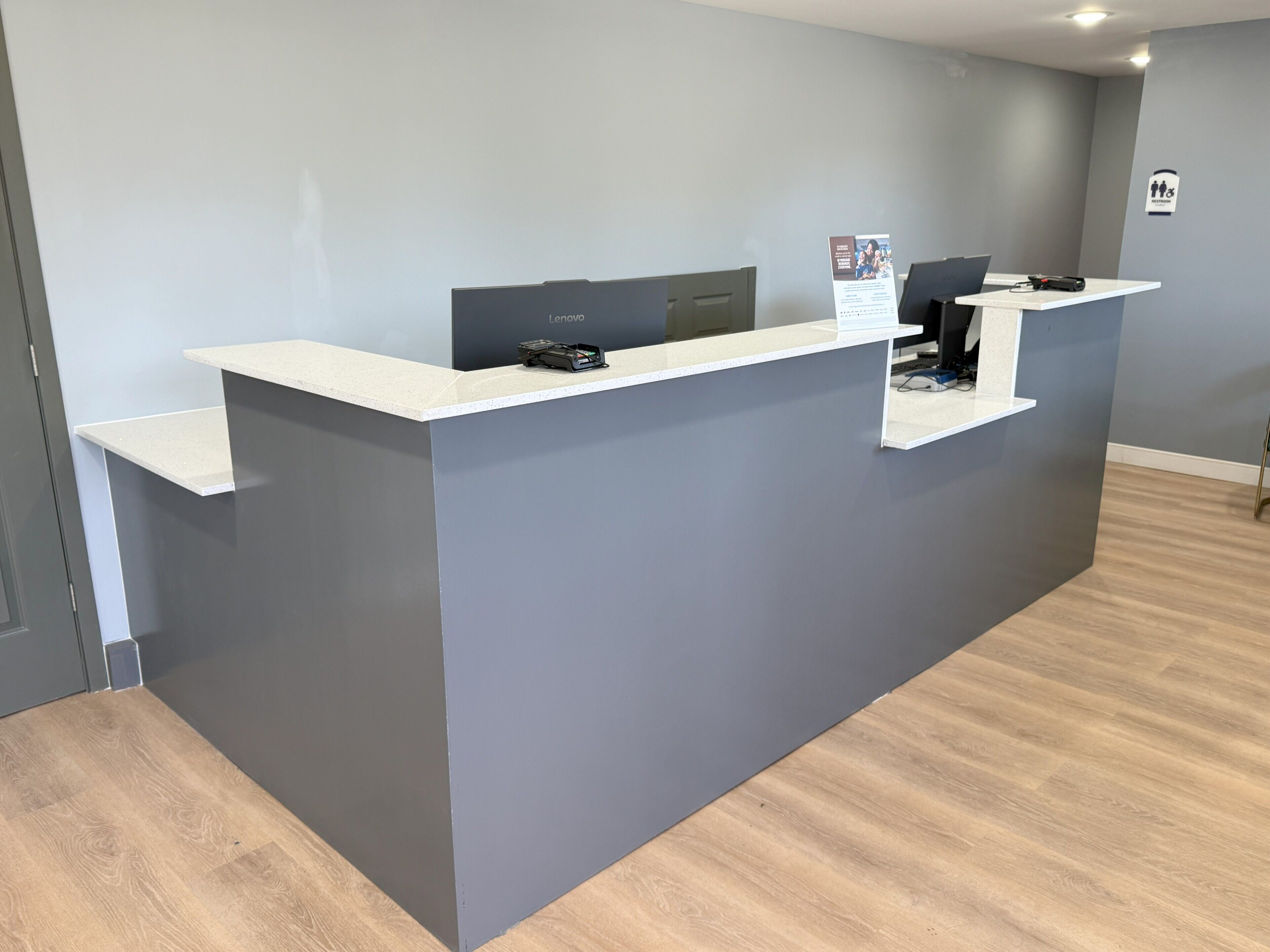 A reception desk with a grey wall and a wooden floor.