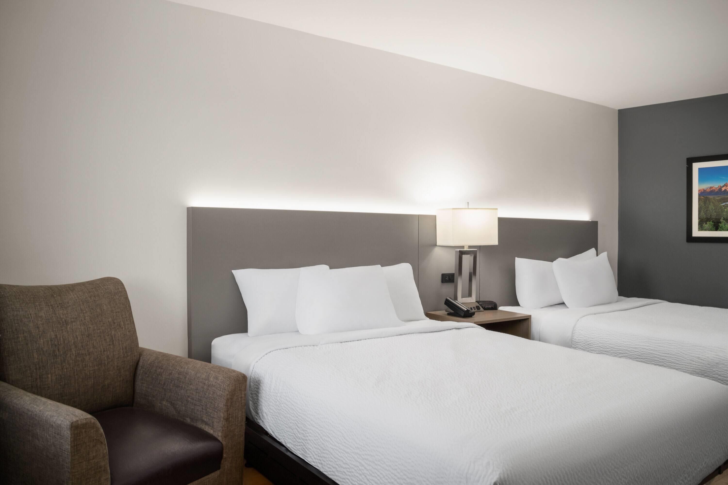 Een hotelkamer met twee bedden, een stoel, een nachtkastje met lamp en een ingelijst schilderij aan de muur.