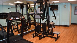 Un gimnasio con máquinas de cardio, máquinas de pesas y un espejo grande.