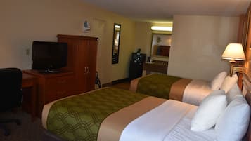 A hotel room with two beds, a desk with a television, a mirror, and a lamp.
