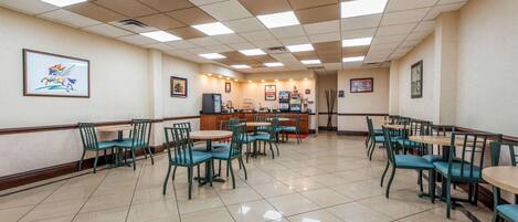 Un amplio comedor con varias mesas y sillas, una barra con el menú, y obras de arte enmarcadas en las paredes.