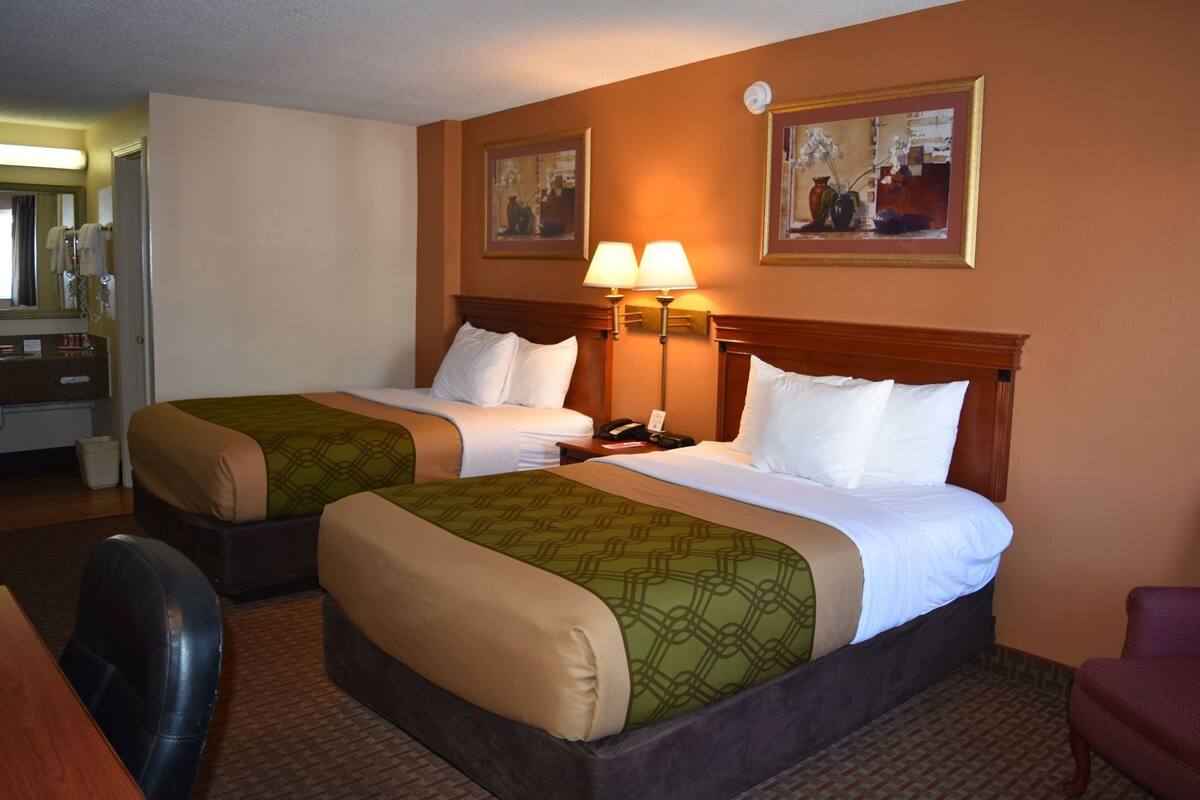 A hotel room with two beds, a desk, a chair, and two lamps.
