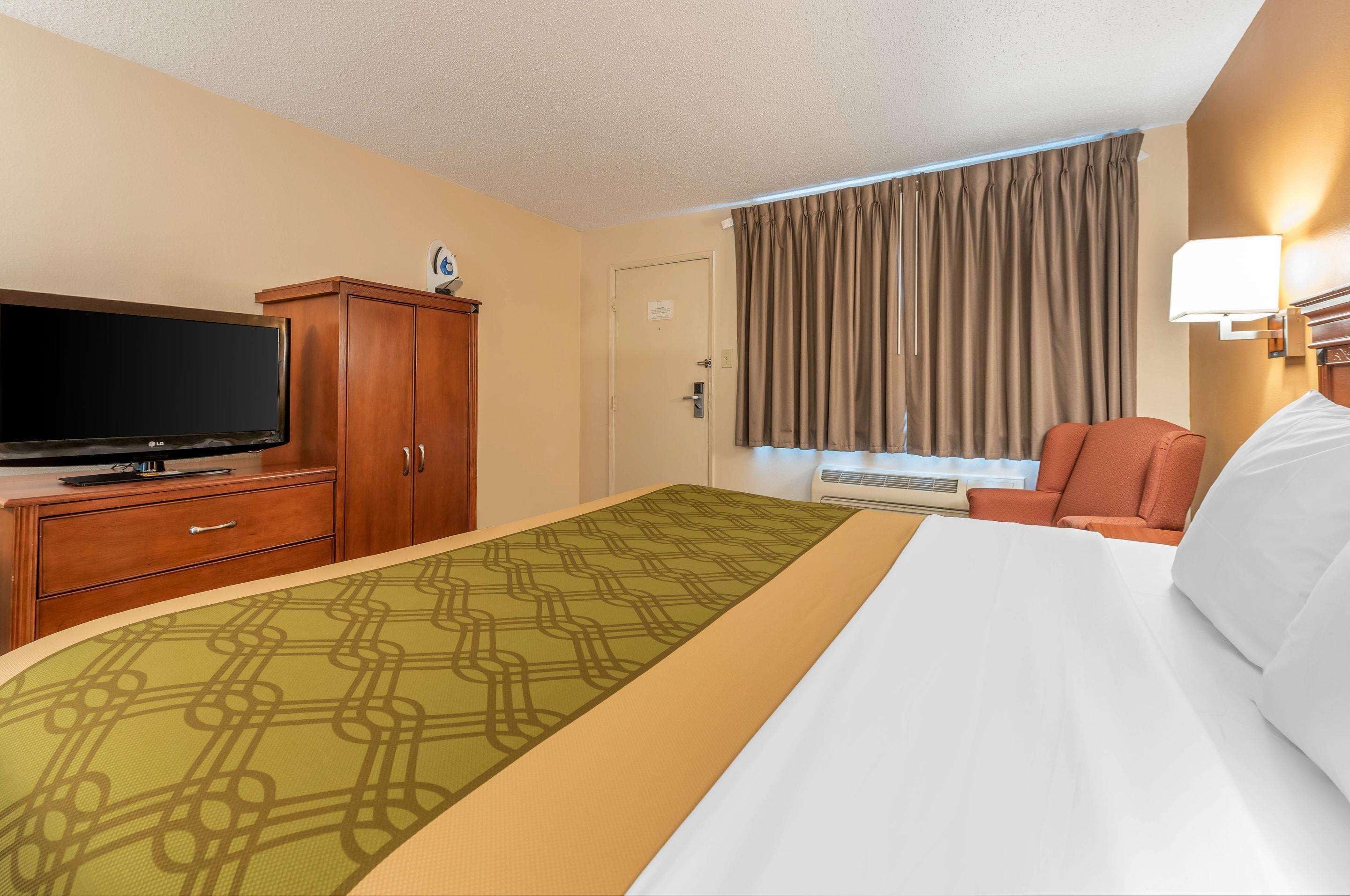 A hotel room with a bed, a television, a desk with a lamp, and a window with curtains.