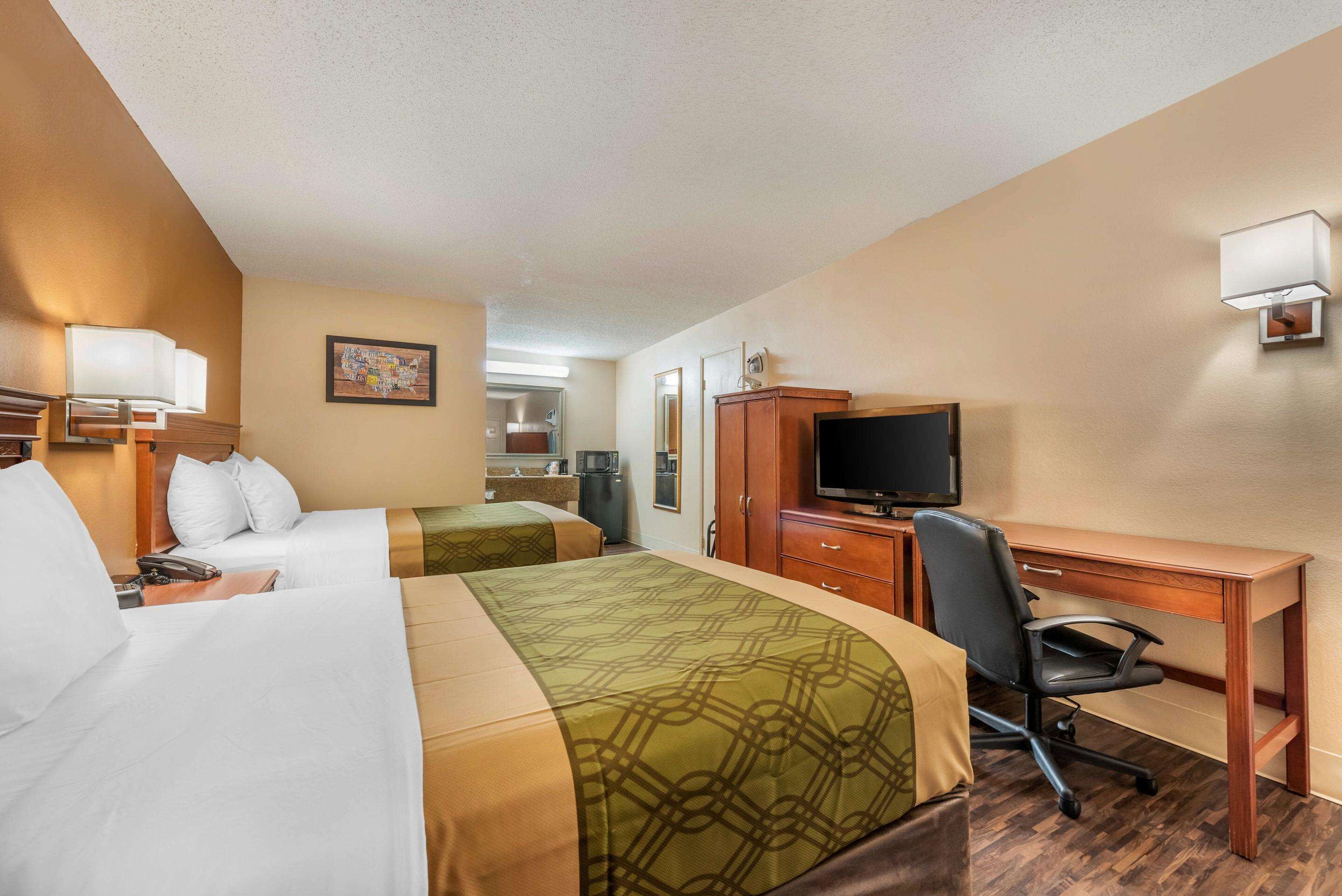A hotel room with two beds, a desk, a chair, a television, and a kitchenette.