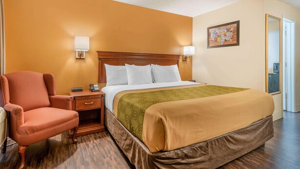 Una habitación de hotel con una cama, una silla, una mesita de noche y una lámpara de pared.