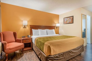Una habitación de hotel con una cama, una silla, una mesita de noche y una lámpara de pared.