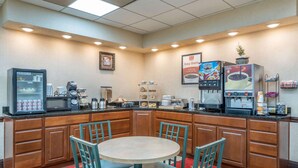 Una cocina de hotel con una mesa redonda y sillas, un refrigerador, máquinas de café y un microondas.
