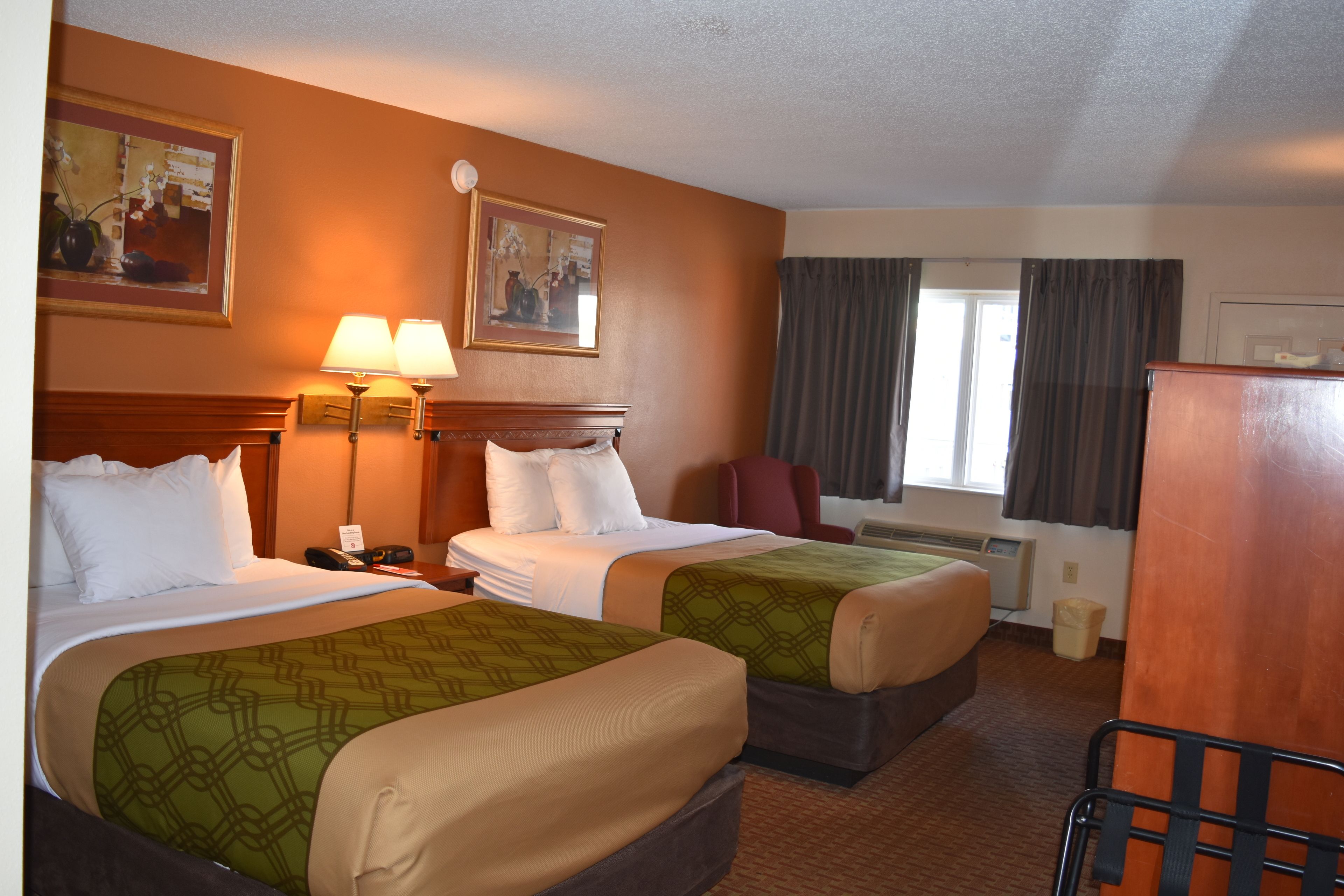 A hotel room with two beds, a desk, a chair, a lamp, and a window with curtains.