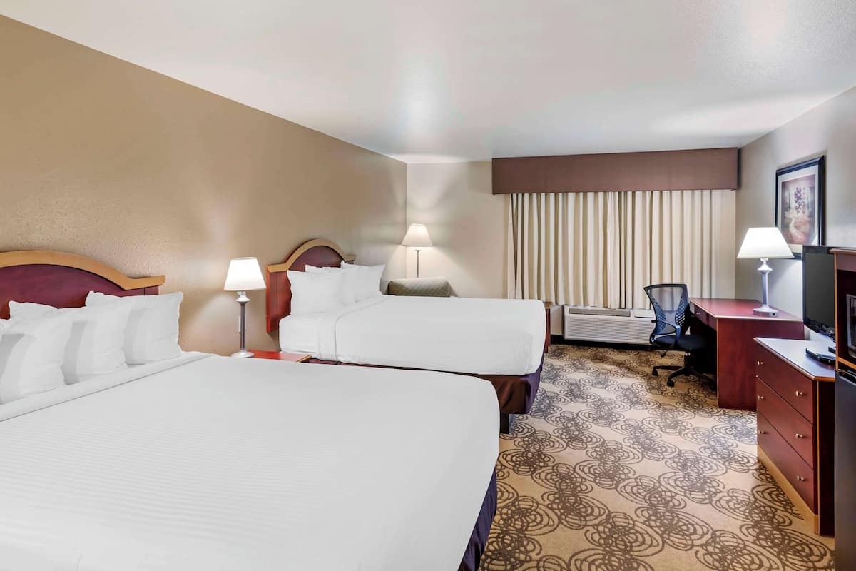 Quarto de hotel com duas camas, uma escrivaninha, uma cadeira e uma televisão.