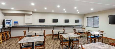 A hotel dining area with tables and chairs, a buffet station, and a television mounted on the wall.