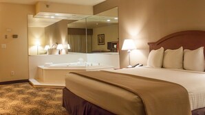 A hotel room with a large bed, a sitting area, a bathroom with a bathtub, and a large mirror.