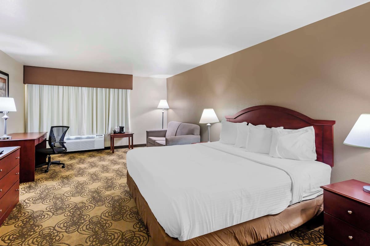 Quarto de hotel com uma cama grande, uma escrivaninha, uma cadeira e uma pequena mesa.