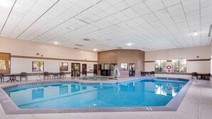 An indoor swimming pool with tiled walls and ceiling, surrounded by seating areas and windows.