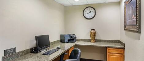 A business center with a desktop computer, printer, and a clock on the wall.