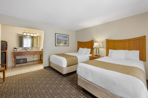 A hotel room with two beds, a desk with a mirror, a picture on the wall, and a patterned carpet.