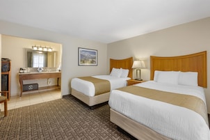 A hotel room with two beds, a desk with a mirror, a picture on the wall, and a patterned carpet.
