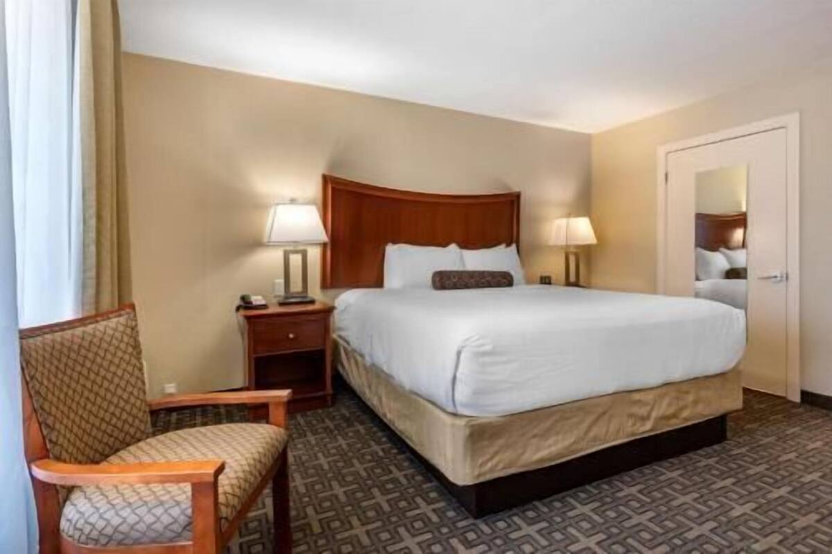 A hotel room with a bed, two bedside tables with lamps, a chair, and a door.