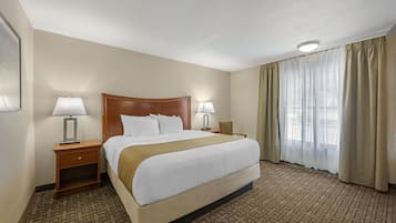 A hotel room with a large bed, two bedside tables with lamps, a window with curtains, and a patterned carpet.