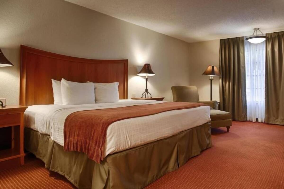 A hotel room with a large bed, a desk, a chair, and a lamp.