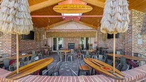 A covered outdoor seating area with tables and chairs, a wooden sign above reading 'OL BARRY'S Surf Club', and a brick wall in the background. - Best Western Swiss Clock Inn (Pecos)
