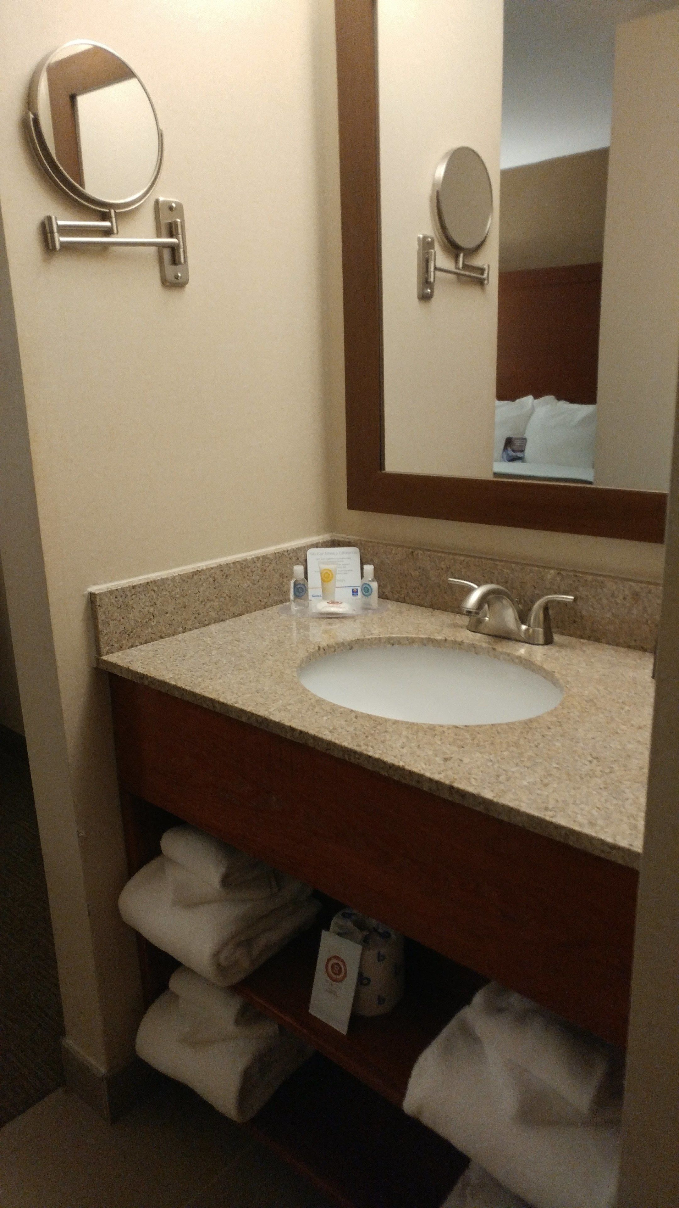 A bathroom with a sink, mirror, towel rack, and a shelf with towels.