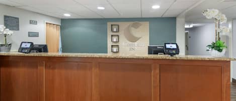 A hotel reception desk with a wooden panel design, a Dell computer, and a potted orchid.