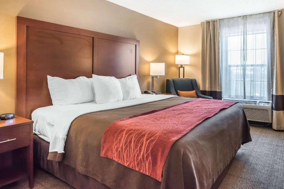 A hotel room with a large bed, a desk, a chair, a window with curtains, and a lamp.