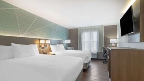 A hotel room with two beds, a desk, a TV, and a large window with curtains.