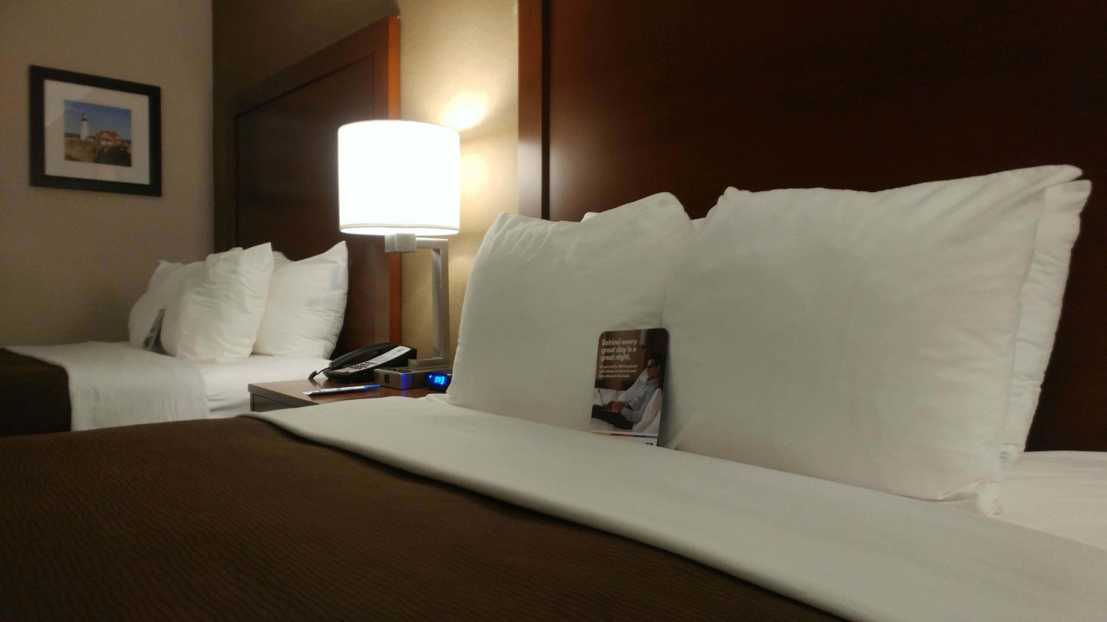 Une chambre d’hôtel avec un lit, des oreillers, une lampe de chevet, un téléphone et un tableau encadré au mur.